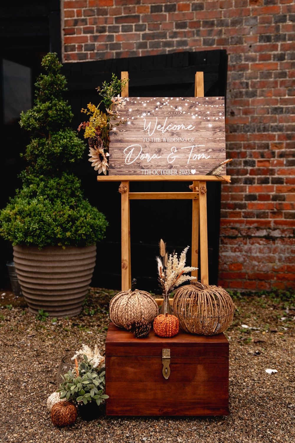 Rustic autumn wedding welcome sign on easel with wicker pumpkins and wooden chest fall decor.