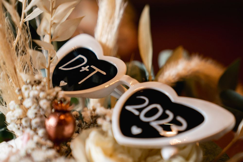 Heart-shaped chalkboard signs reading D+T and 2023 nestled in a rustic dried floral wedding arrangement.
