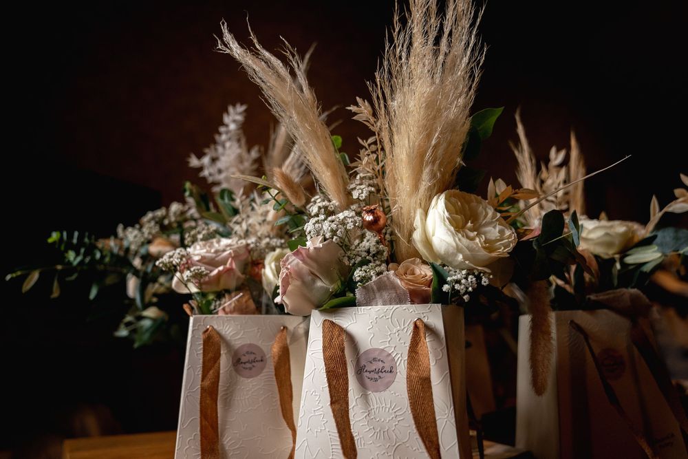 Elegant wedding favor bags decorated with pampas grass, roses, and dried flowers on a table.