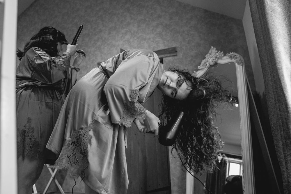 Black and white photo of bride having her curly hair styled before her wedding ceremony.
