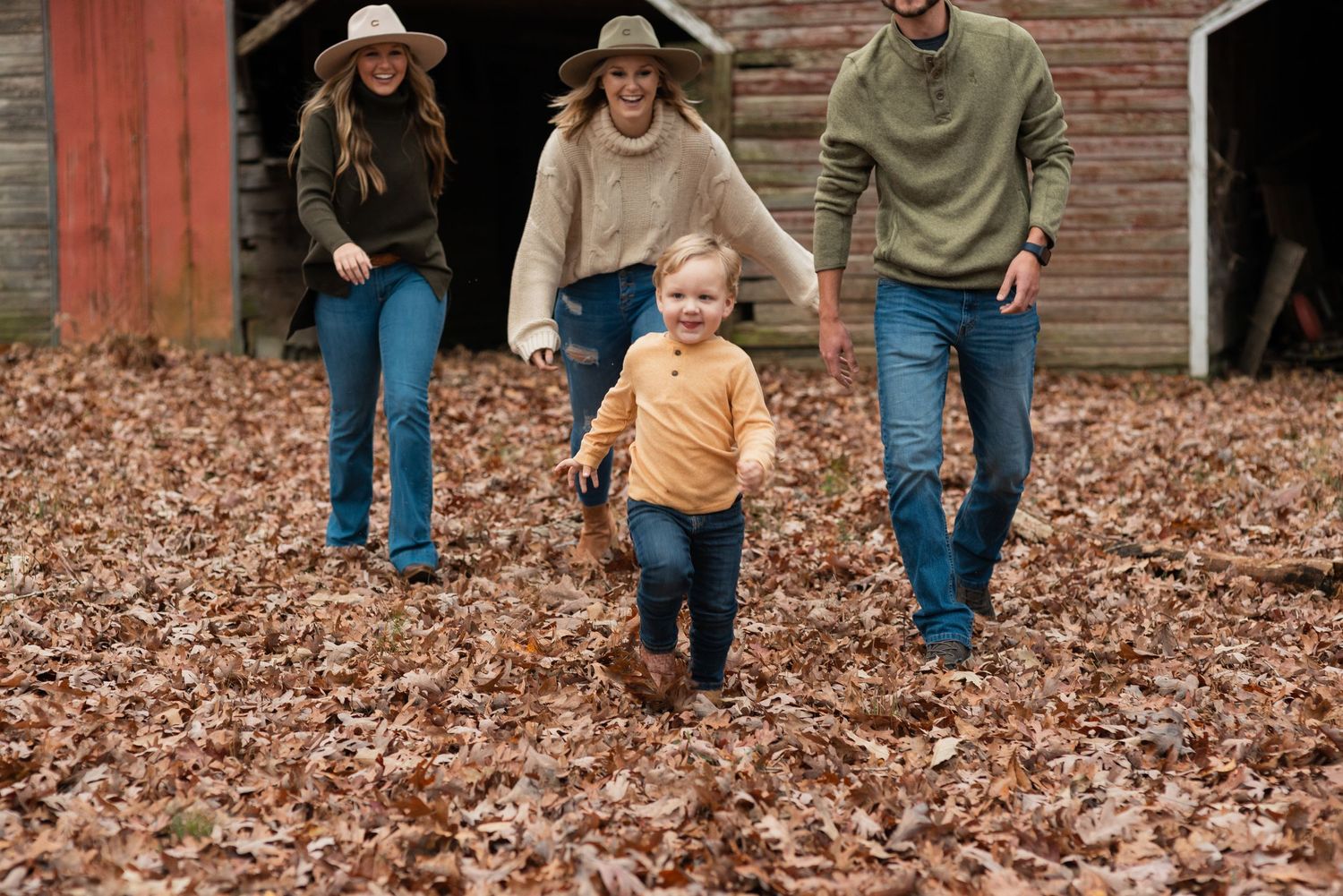 young boy running in front of family in thick fallen leaves