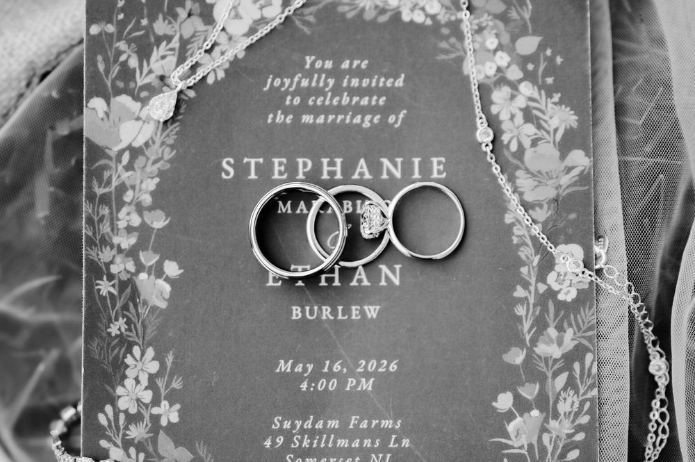 Black and white wedding invitation for Stephanie and Ethan Burlew with two wedding rings resting on top.