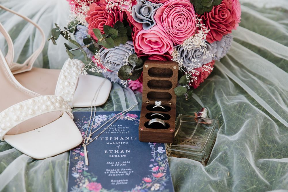 Wedding flat lay with pink floral bouquet, rings in wooden box, heels, and navy floral invitation for Stephanie and Ethan.
