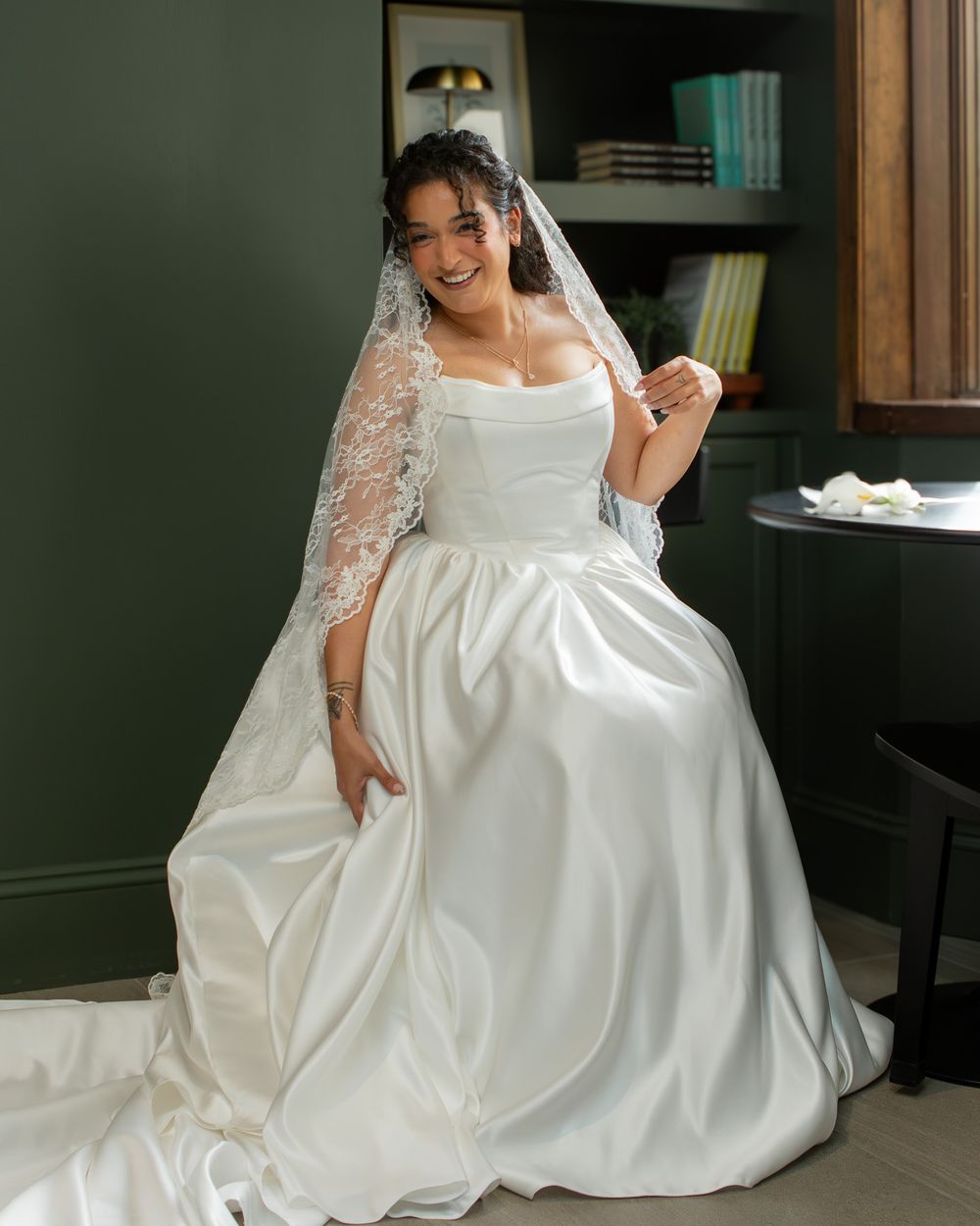 Bride in a satin gown with a trailing lace veil laughing in her bridal suite before her ceremony in Lakewood.