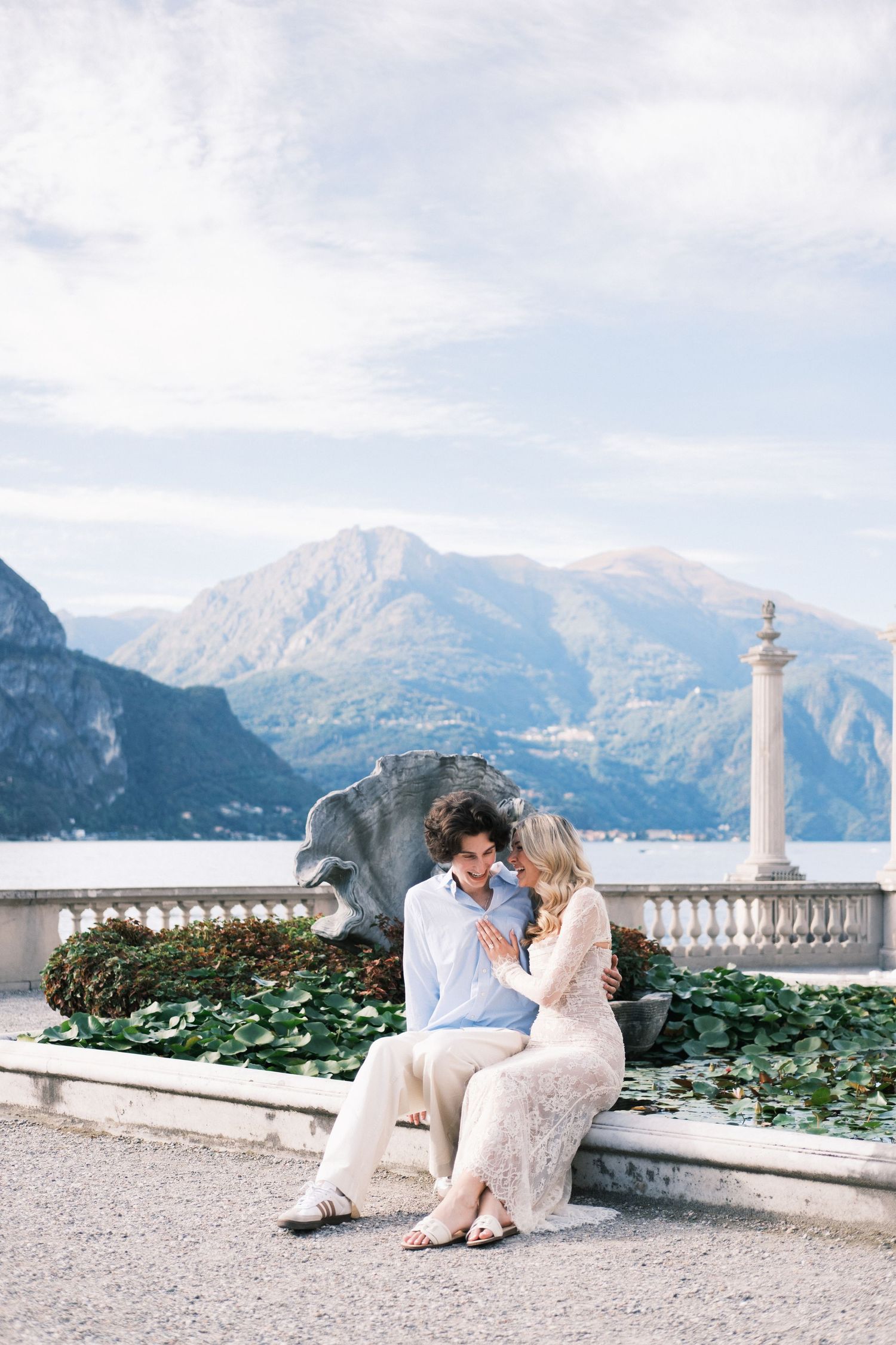 Couple sitting together by a fountain with Lake Como and mountain backdrop in Italy.