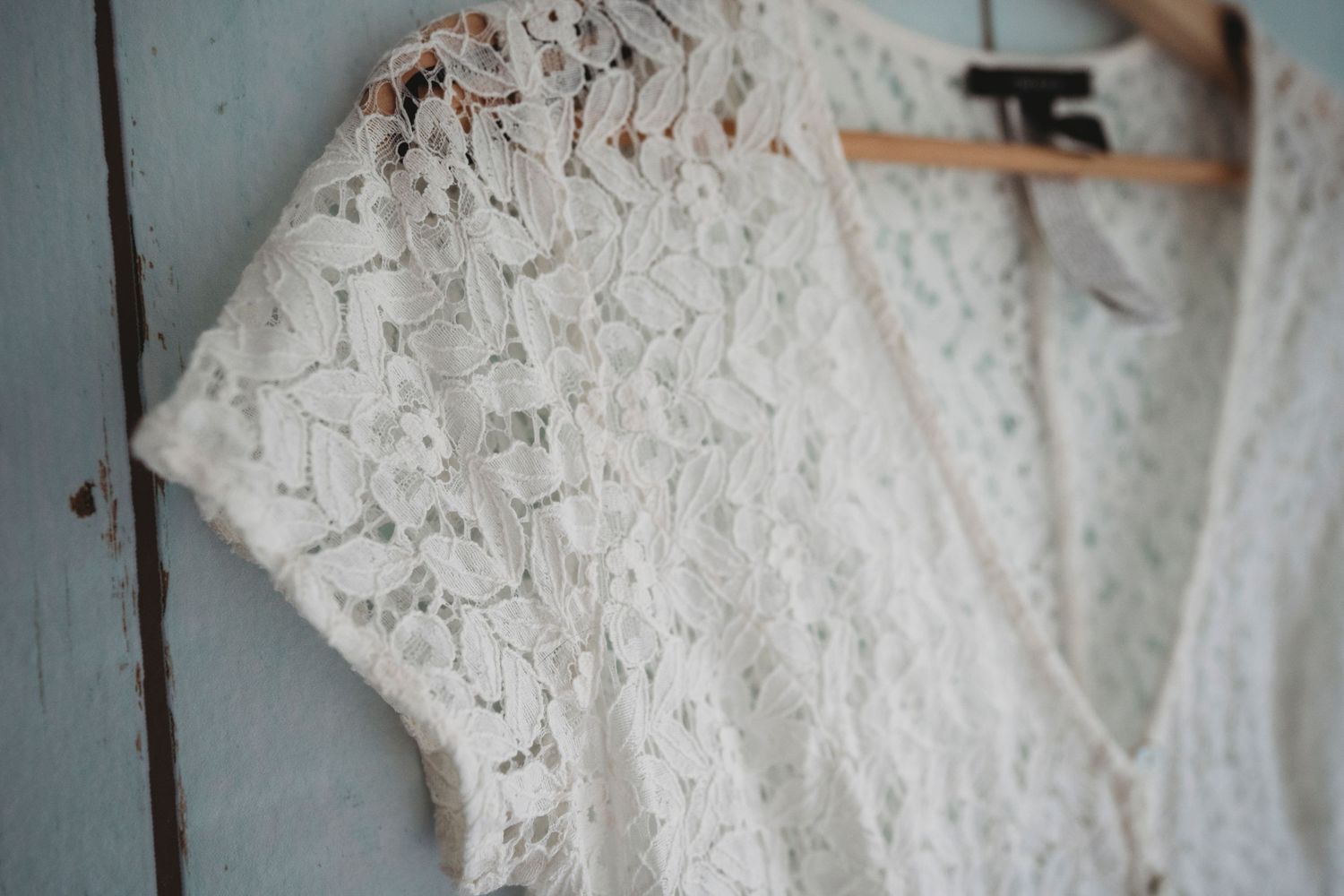 Close up detail of delicate white lace on vintage dress hanging on door.