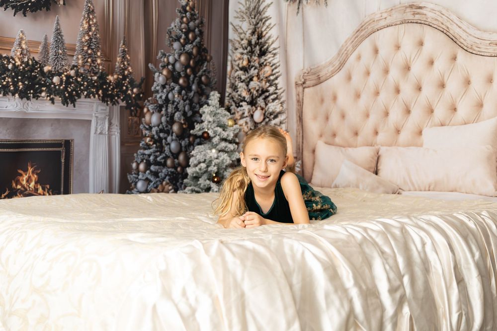 Young girl in black dress lying on elegant bed with Christmas trees and fireplace in festive holiday room.