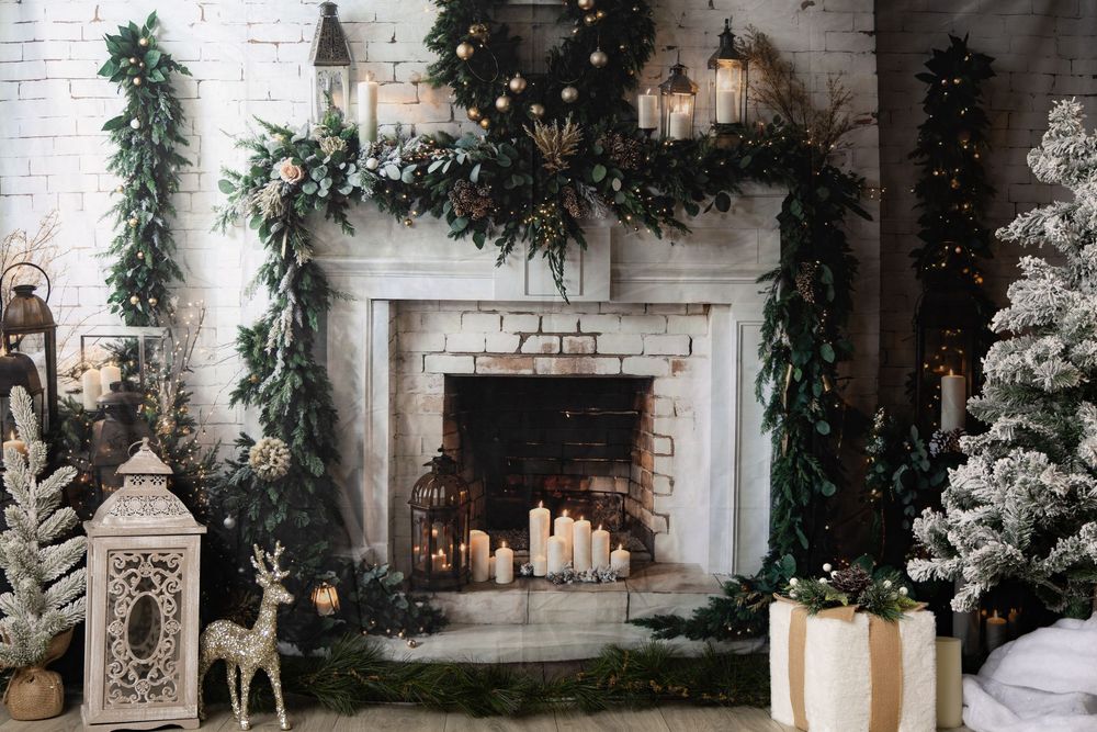 White brick fireplace decorated with Christmas garland, candles, lanterns, and a gold reindeer figurine beside a flocked tree.