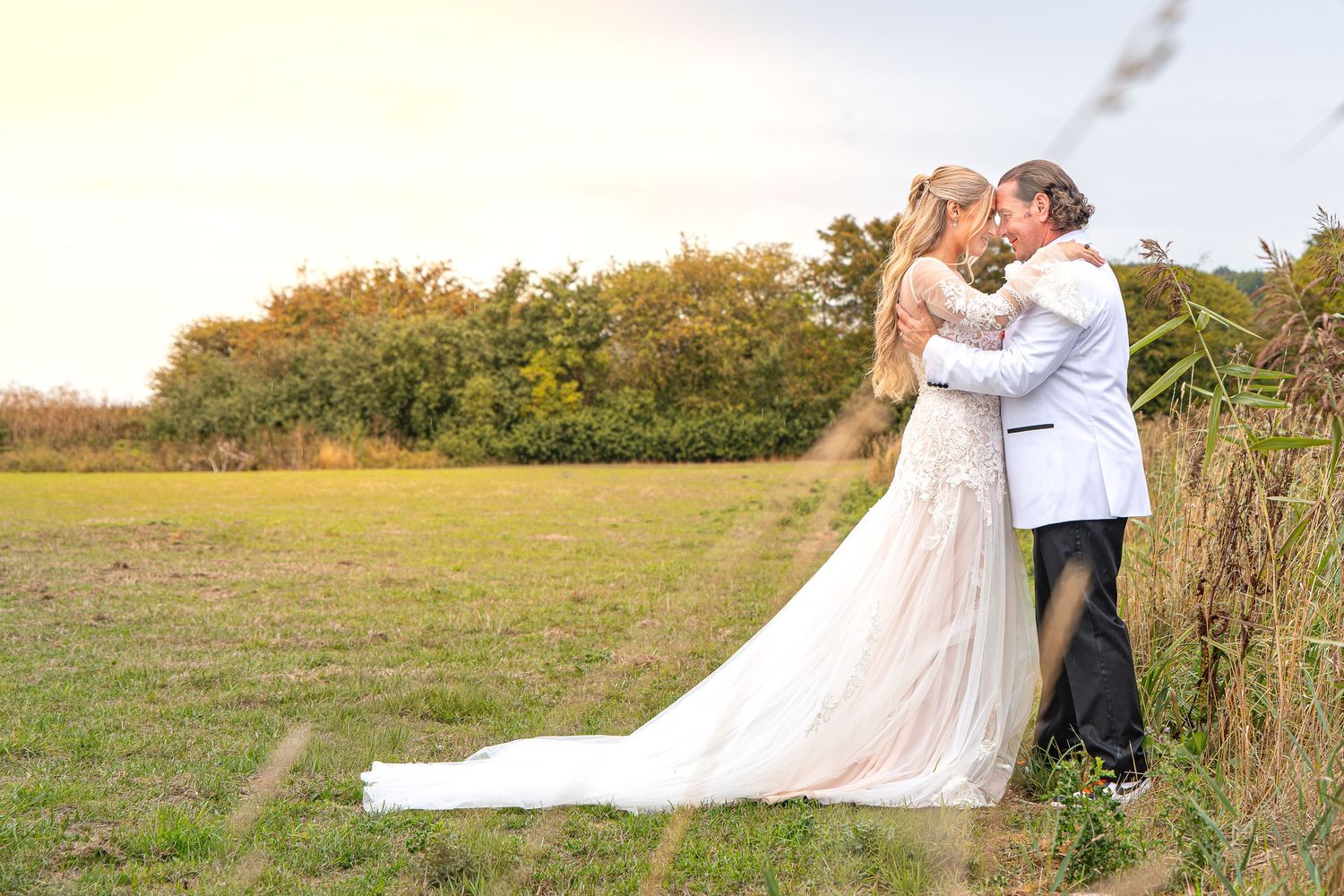 Bride and groom dip kiss in field with colorful orange and gray smoke bombs during outdoor wedding photo shoot.