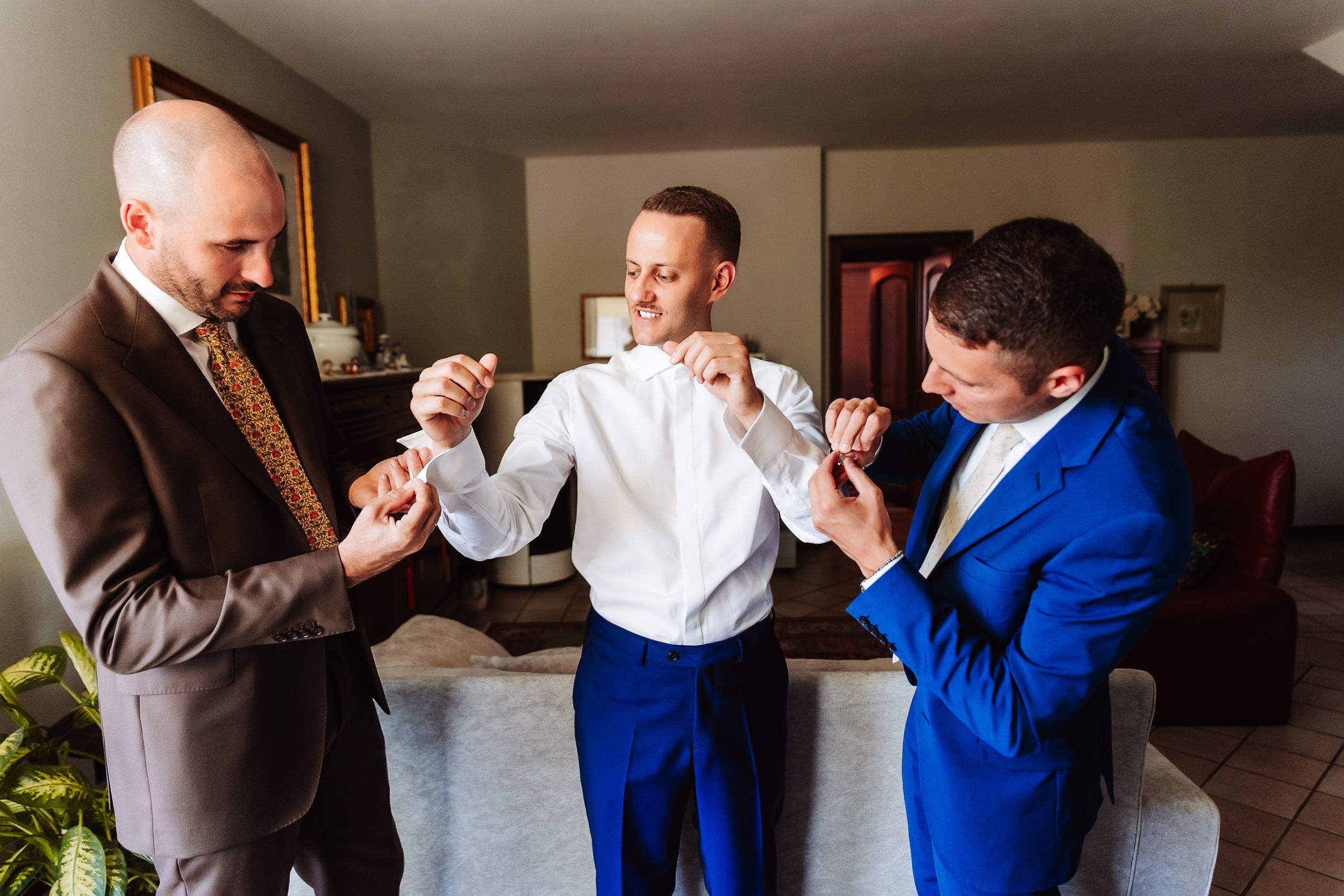 Groom and groomsmen adjusting suits before wedding ceremony indoors.
