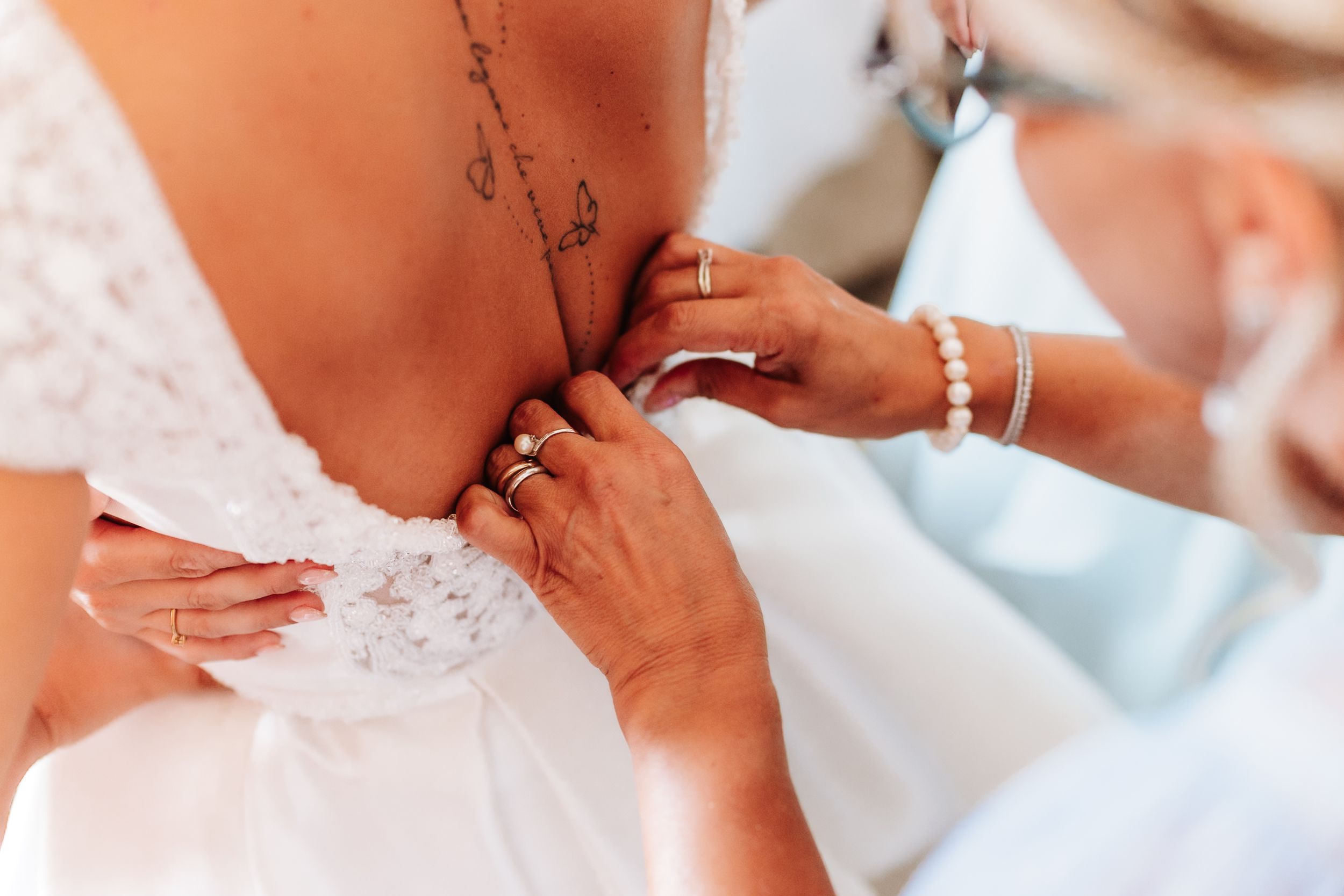 Close-up of hands buttoning the back of a white lace wedding dress on a bride.