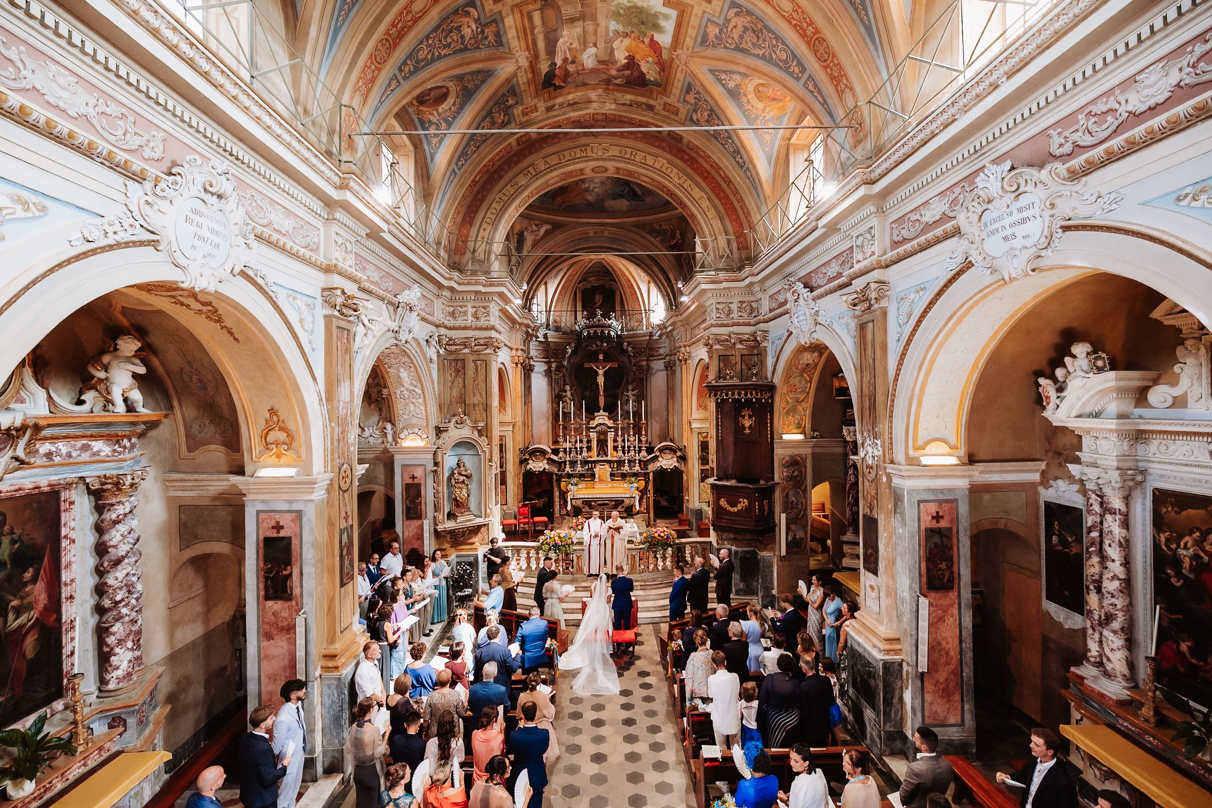 Elegant wedding ceremony inside an ornate Italian baroque church with frescoed ceilings and guests filling the pews.
