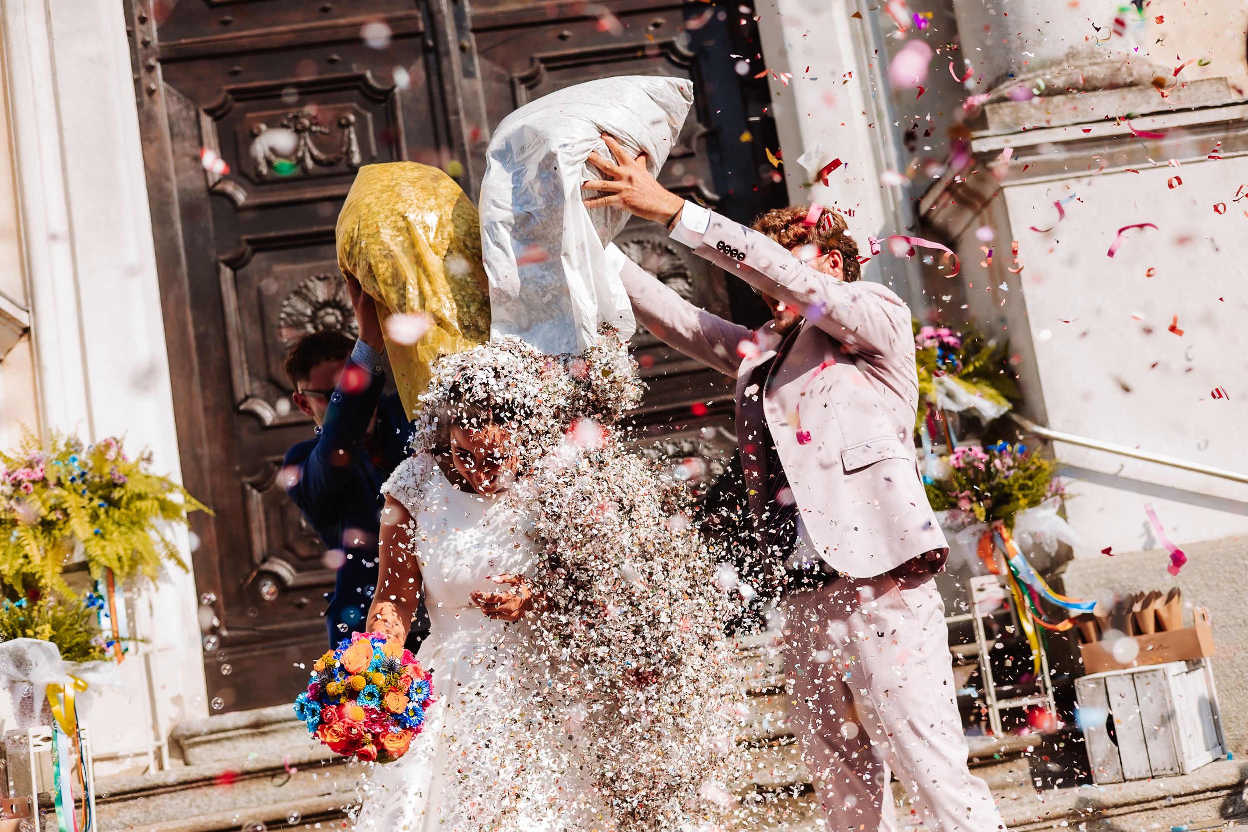 Bride and groom celebrate outside church doors showered with colorful confetti.