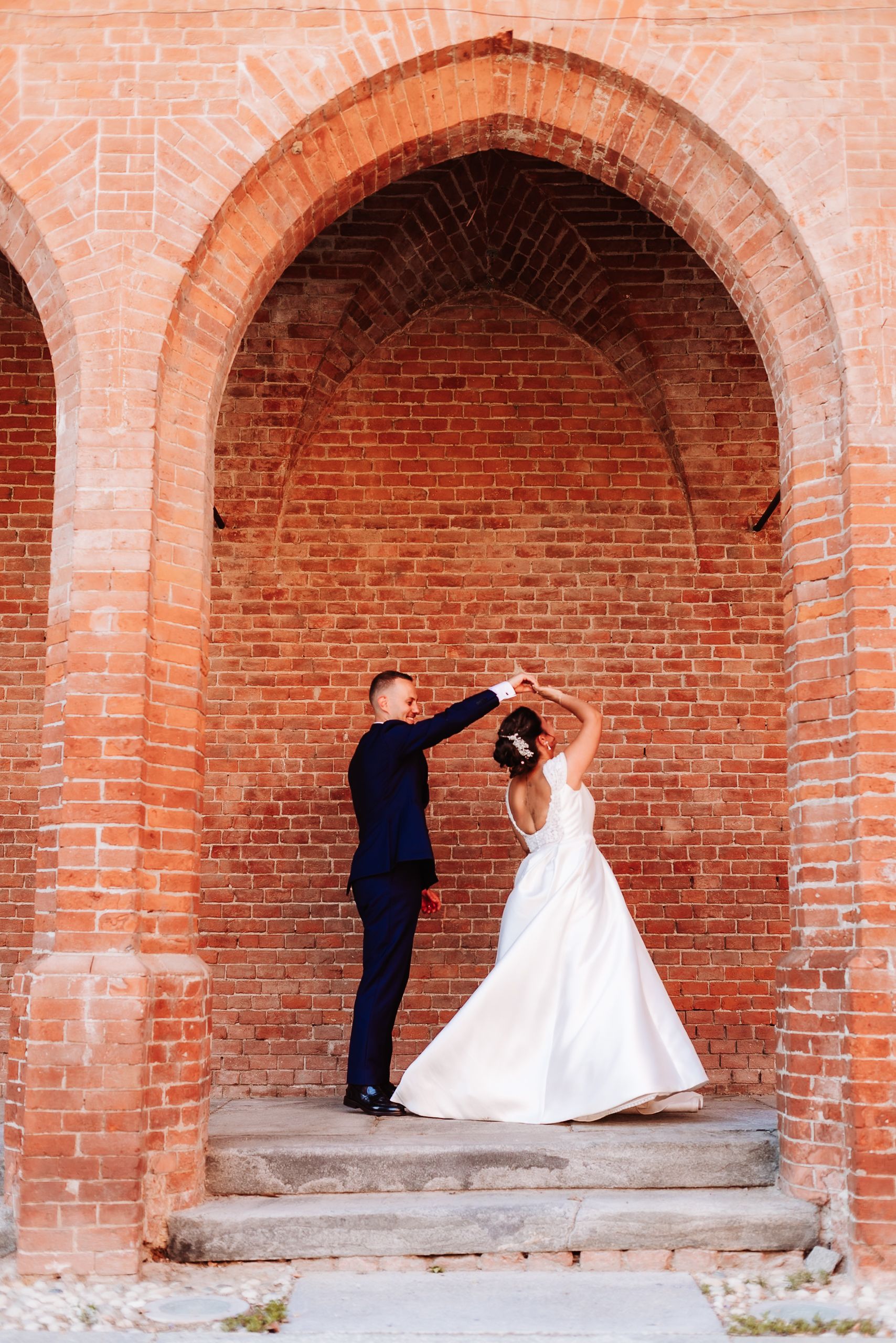 Bride and groom dance together in a rustic red brick arched doorway.