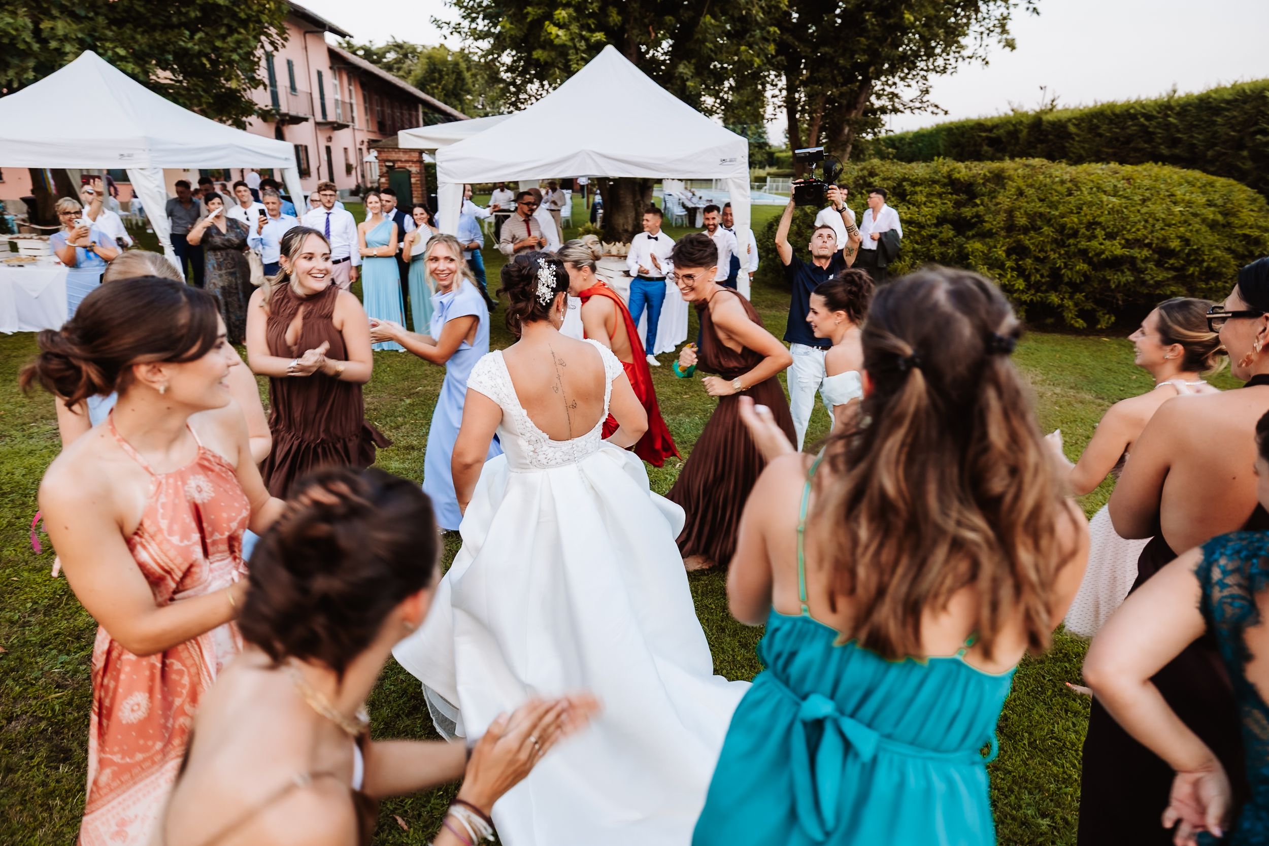 Wedding guests dancing outdoors at a garden reception, with bride in white gown surrounded by celebrating friends.