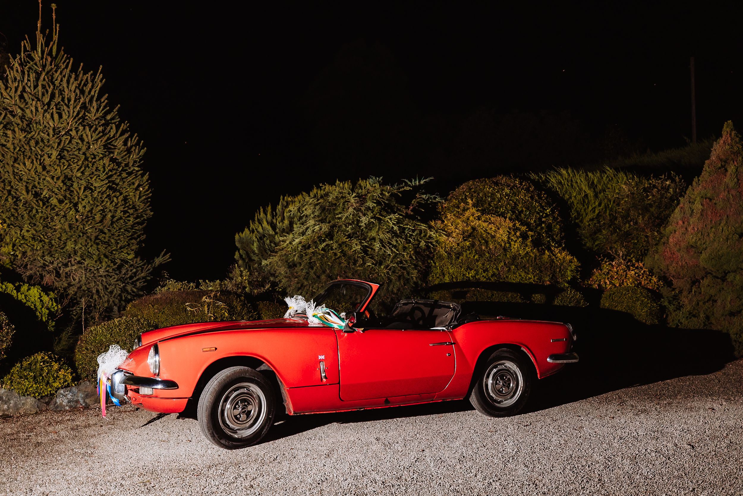 Classic red vintage convertible sports car decorated with wedding flowers parked at night outdoors.