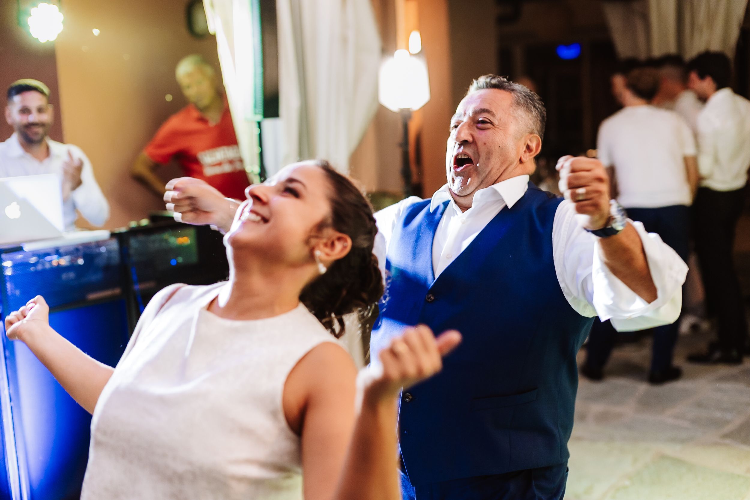 Bride and older man dancing joyfully at a wedding reception, both laughing and celebrating on the dance floor.