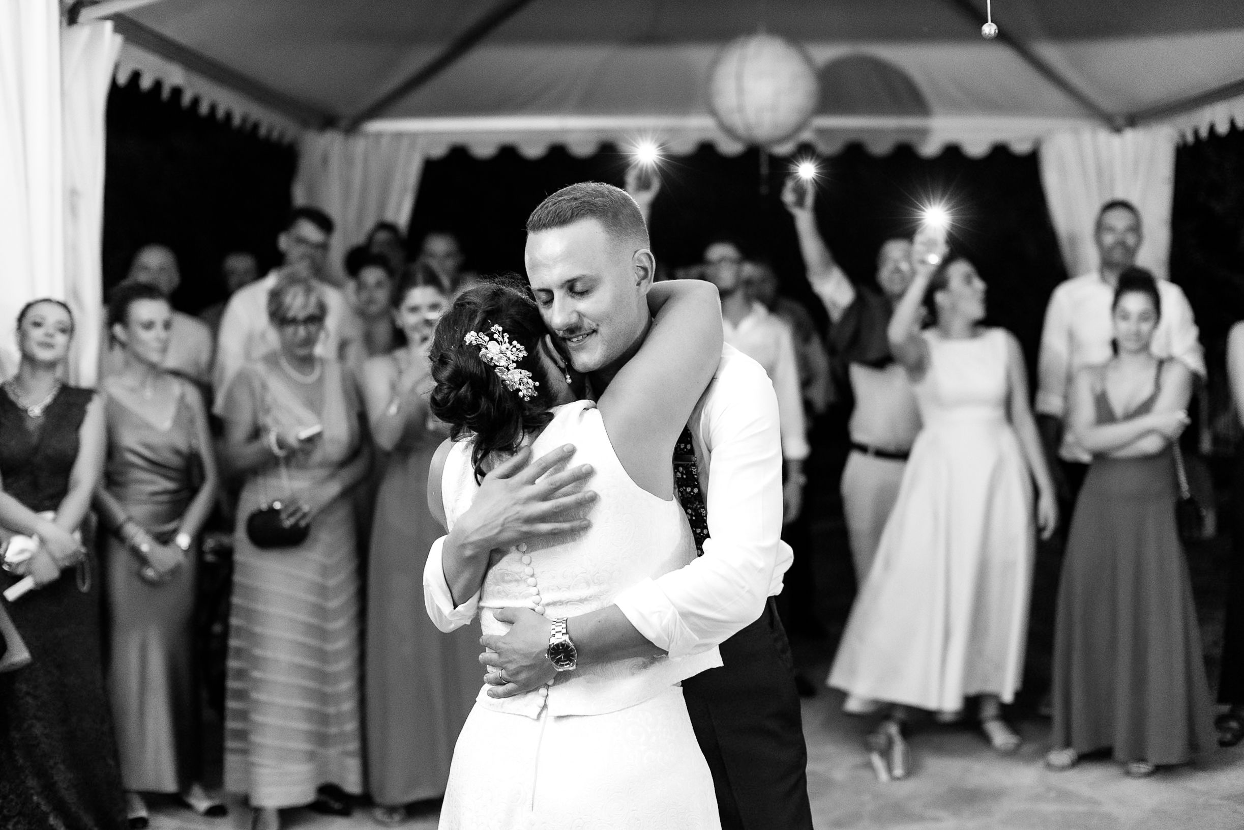 Black and white photo of bride and groom sharing first dance at wedding reception with guests watching.