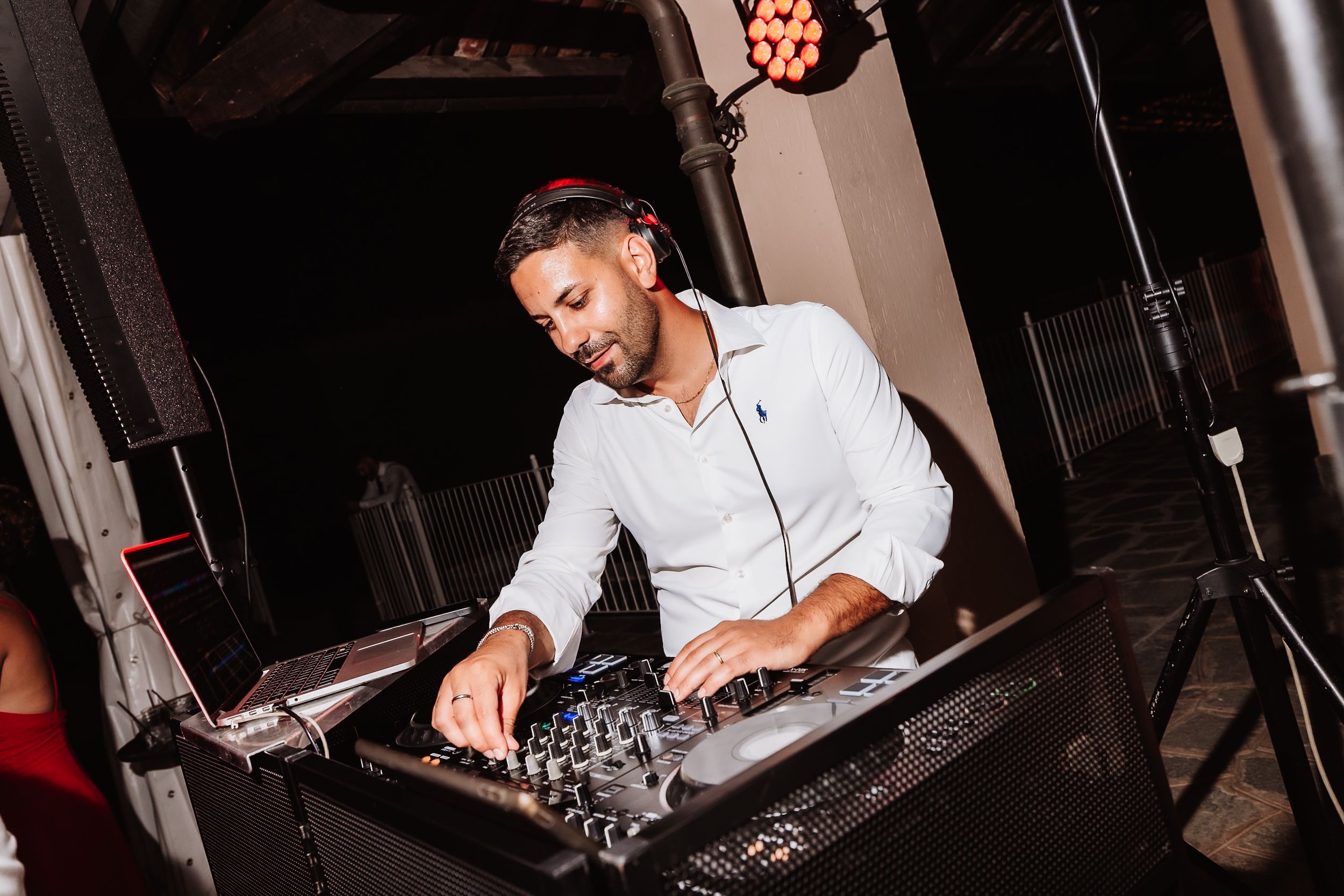 DJ mixing music at a nighttime event, wearing a white shirt and operating a professional audio mixer.