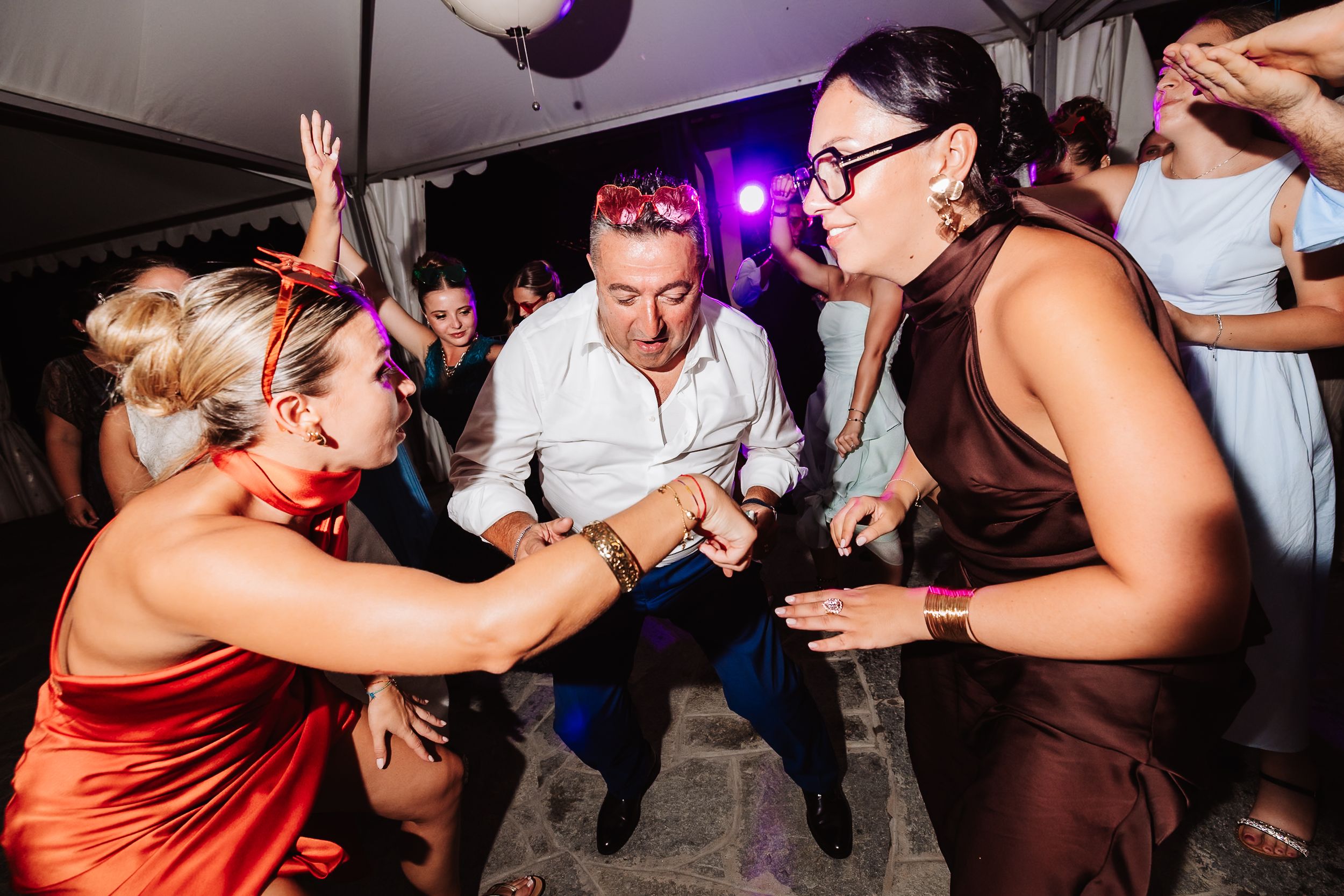 Guests dancing energetically at a lively wedding reception party under colorful lights.