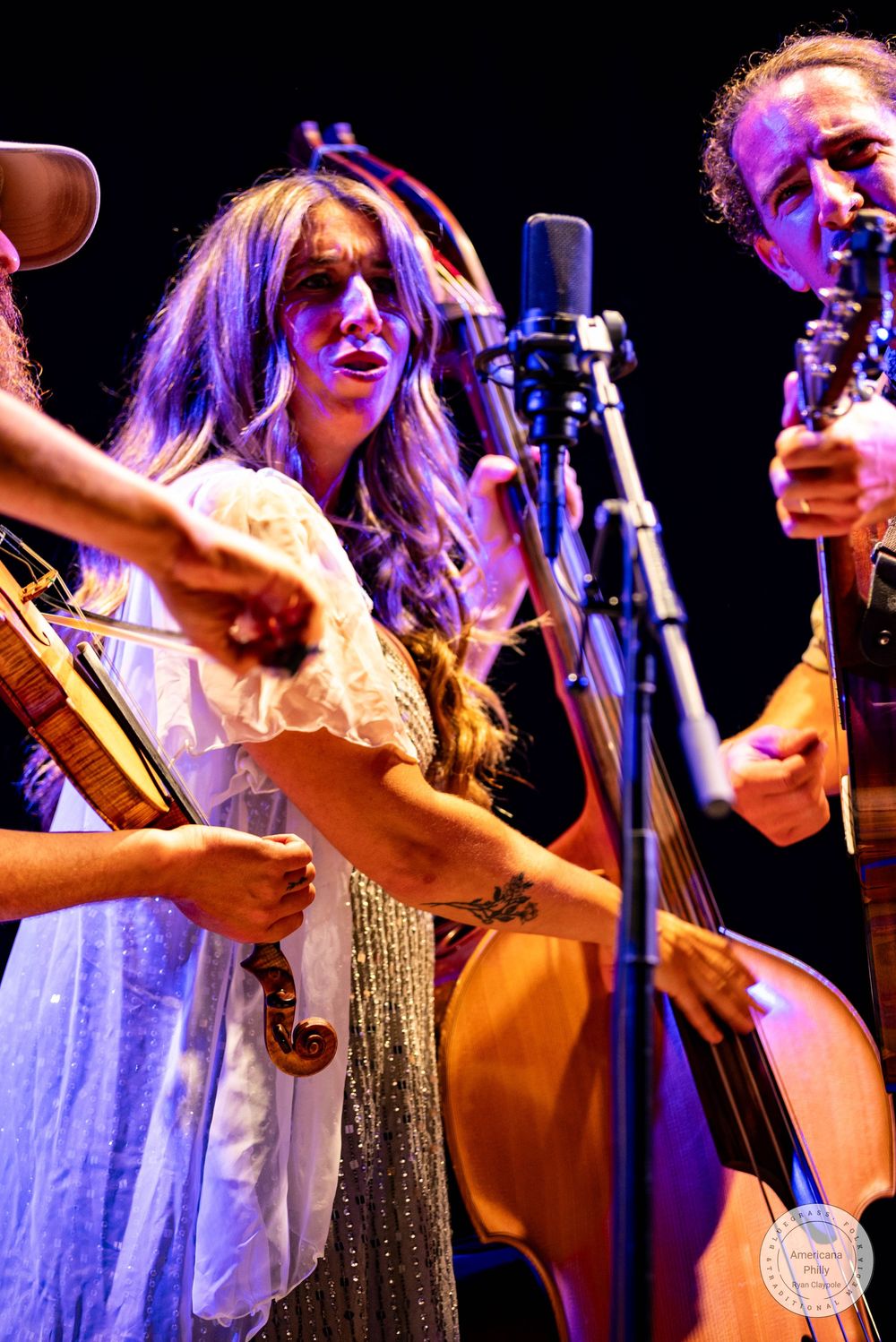 Female vocalist performing on stage with violin and upright bass players in a live bluegrass concert.