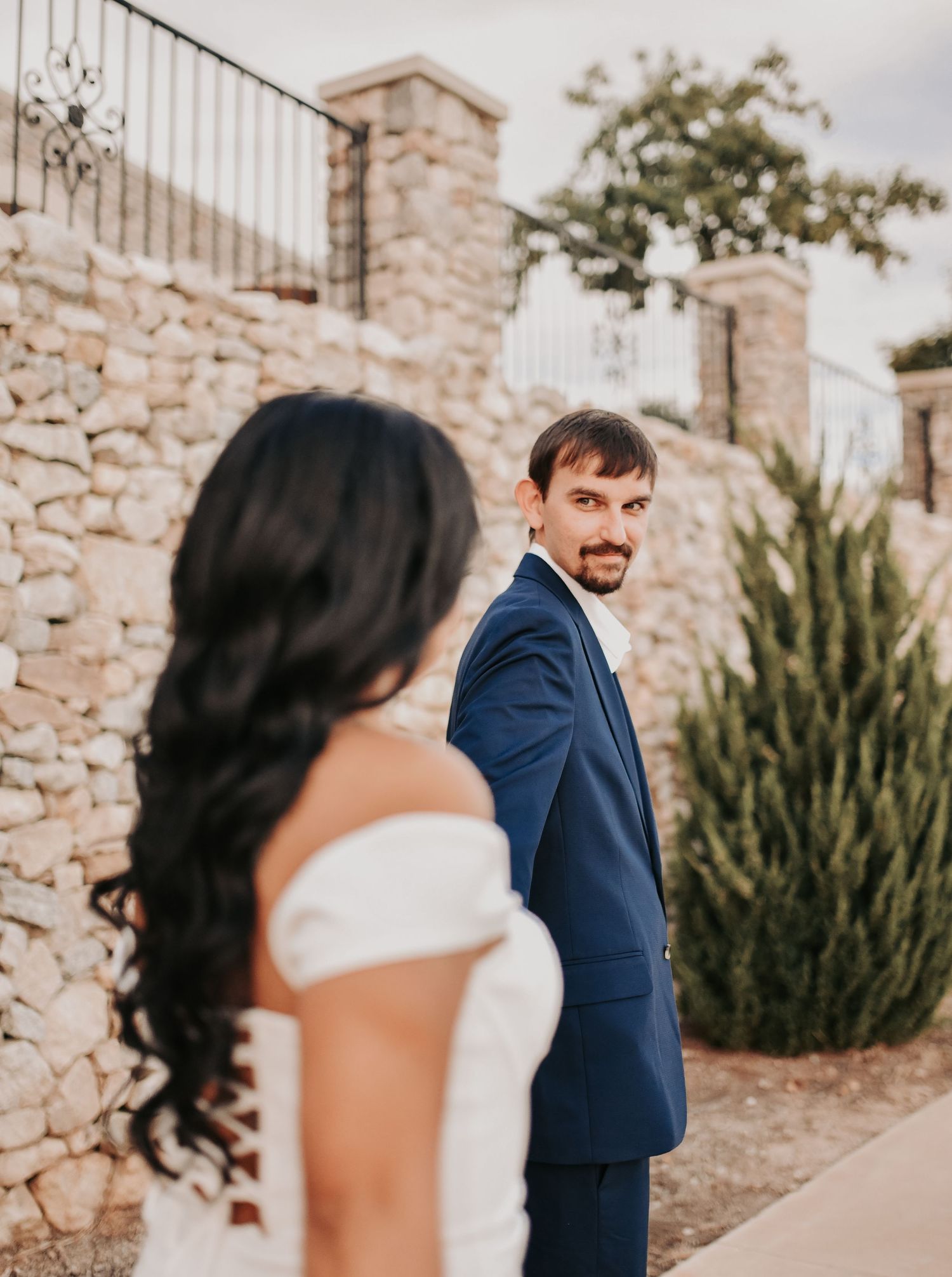 Bride-to-be lifting her white dress as she walks beside her fiancé near the water