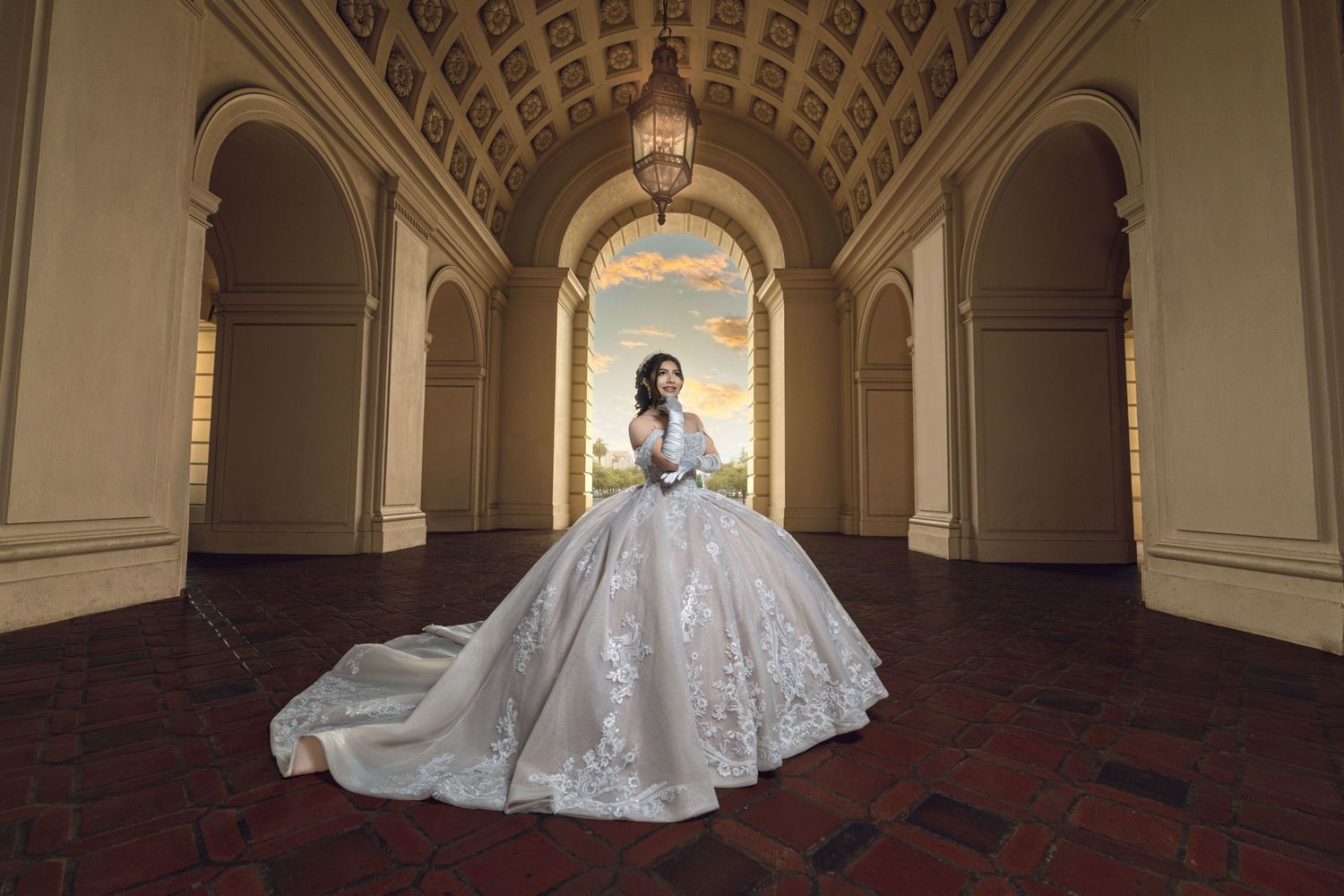 Bride in a stunning ball gown wedding dress poses in an elegant archway with ornate ceilings and warm chandelier lighting.
