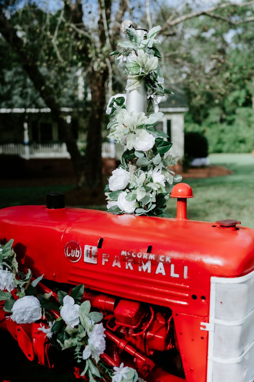 Red McCormick Farmall Cub tractor decorated with white roses and greenery garland for a rustic outdoor wedding.