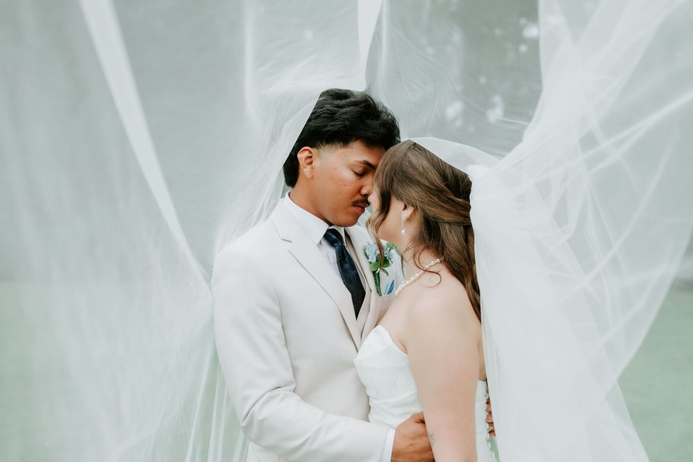 A bride and groom share an intimate moment under a flowing white veil on their wedding day.