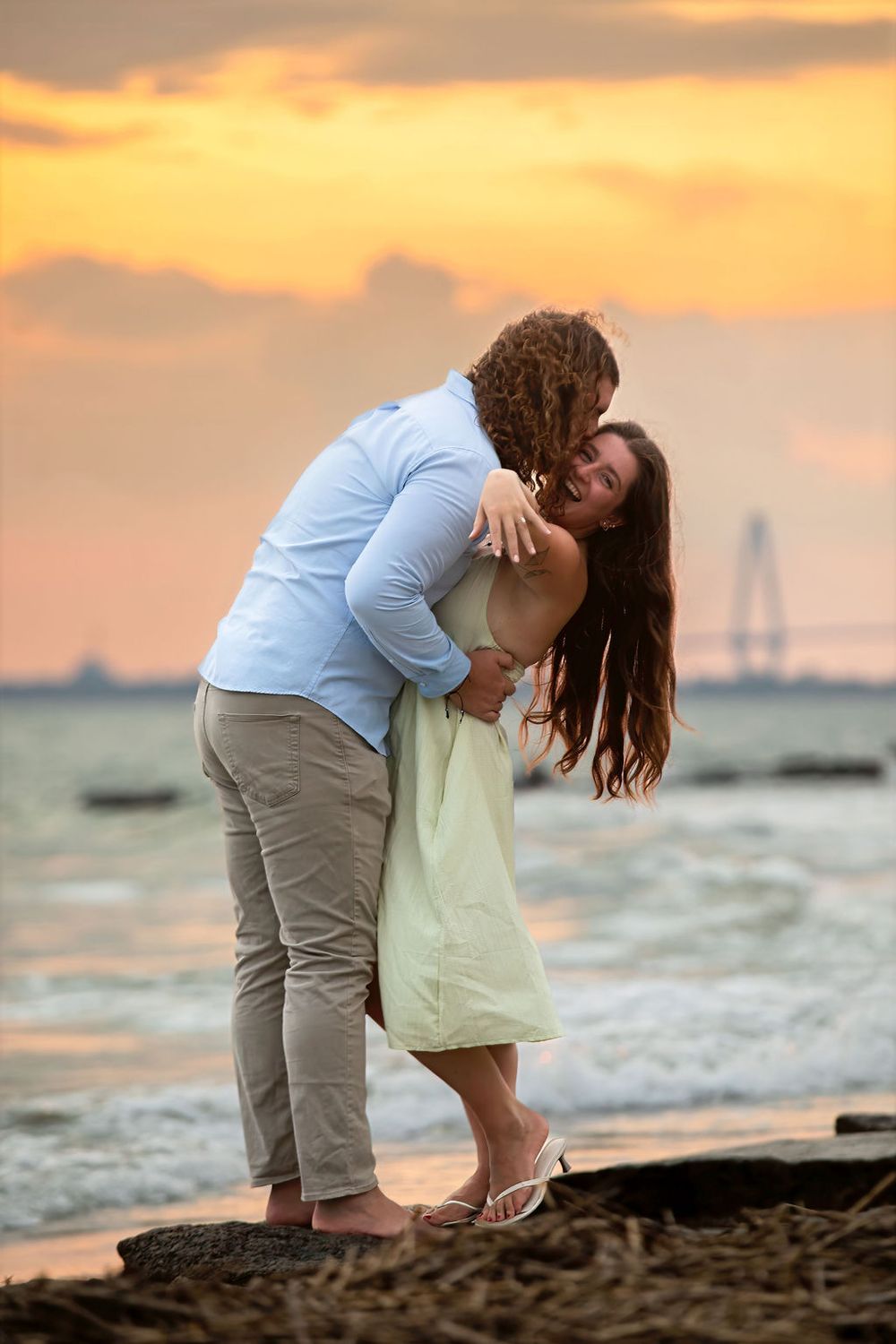 Couple embracing romantically on a beach at sunset, with golden skies and ocean waves in the background.