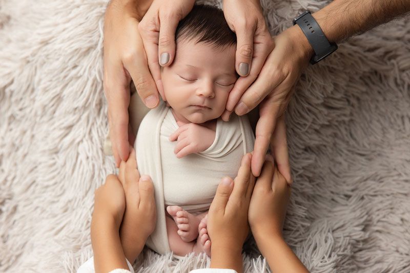 Newborn baby peacefully sleeping while two parents gently cradle the infant with their hands on a soft fur blanket.