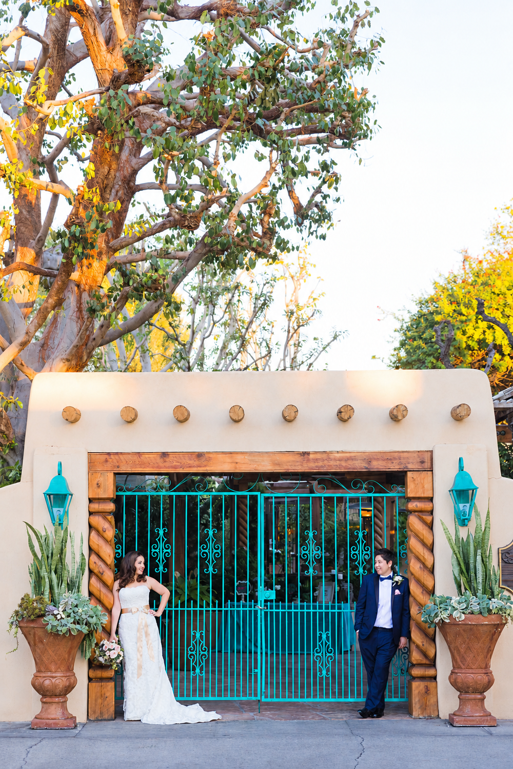 Bride and groom stand apart at a turquoise iron gate entrance of a Spanish-style wedding venue.
