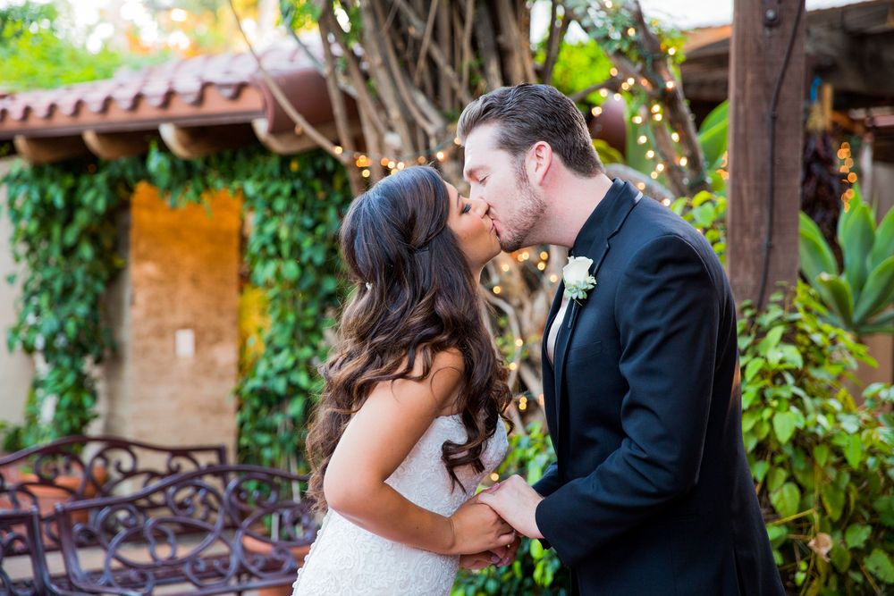 Bride and groom share a romantic kiss surrounded by lush green ivy at their outdoor wedding venue.