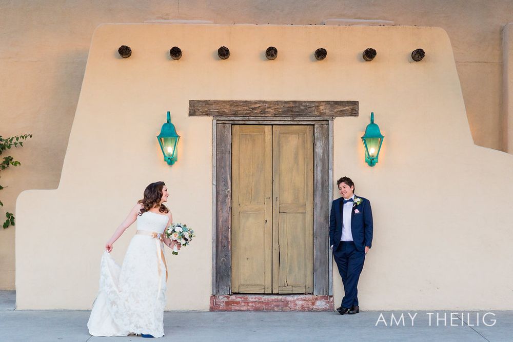 Bride and groom pose apart near a rustic adobe wall with turquoise lanterns at sunset wedding.