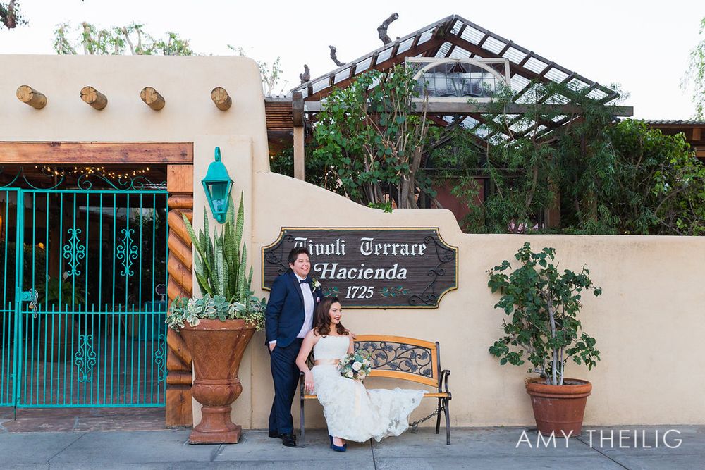 Bride and groom sitting on bench by Tivoli Terrace Hacienda 1725 sign at wedding venue.