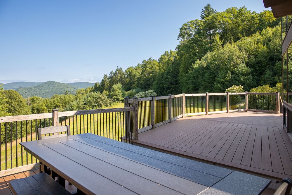Expansive wood deck with dining table overlooking stunning mountain valley and blue sky views.