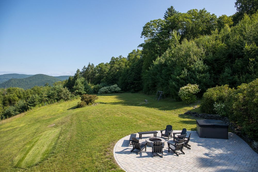 Patio with Adirondack chairs arranged around fire pit with sweeping mountain landscape views.