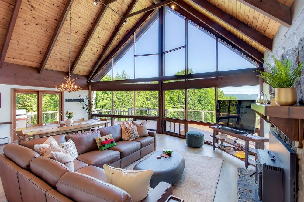 Spacious chalet living room with vaulted wood ceiling and floor-to-ceiling windows overlooking mountains.