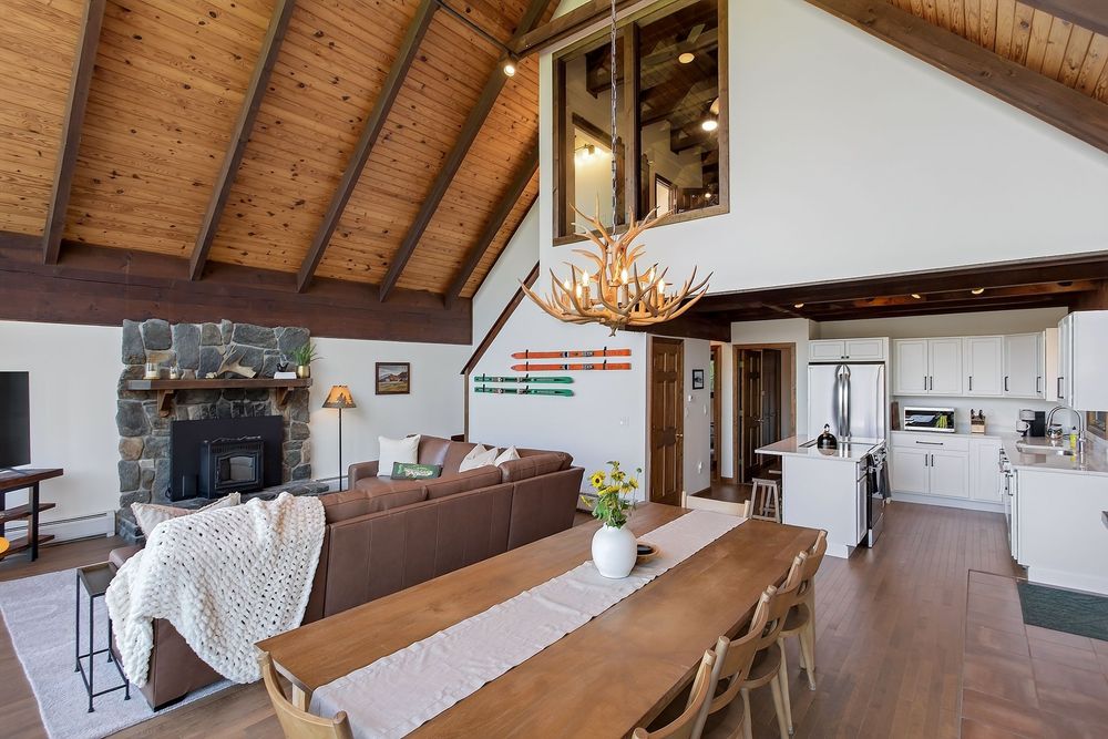 Open-plan rustic chalet interior with stone fireplace, dining area, and modern kitchen.