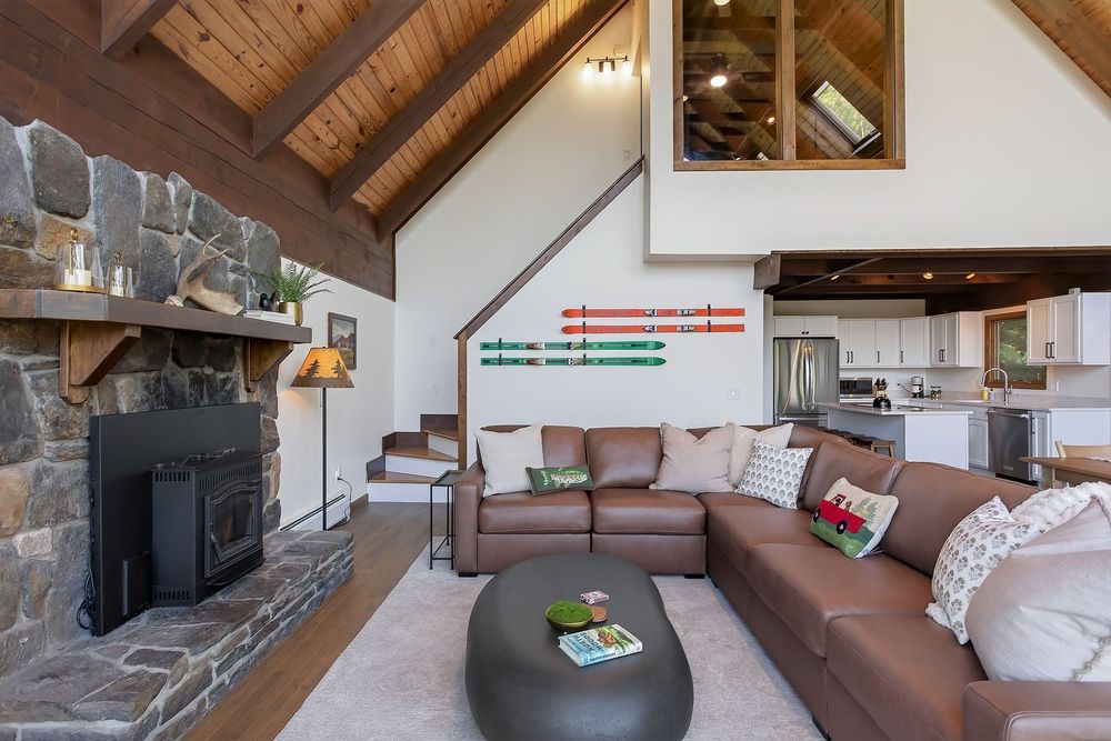 Cozy living room with leather sectional sofa, stone fireplace, and vaulted wood-beamed ceiling.