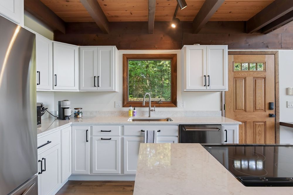 White kitchen with quartz countertops, stainless appliances, wood beam ceiling, and garden window.