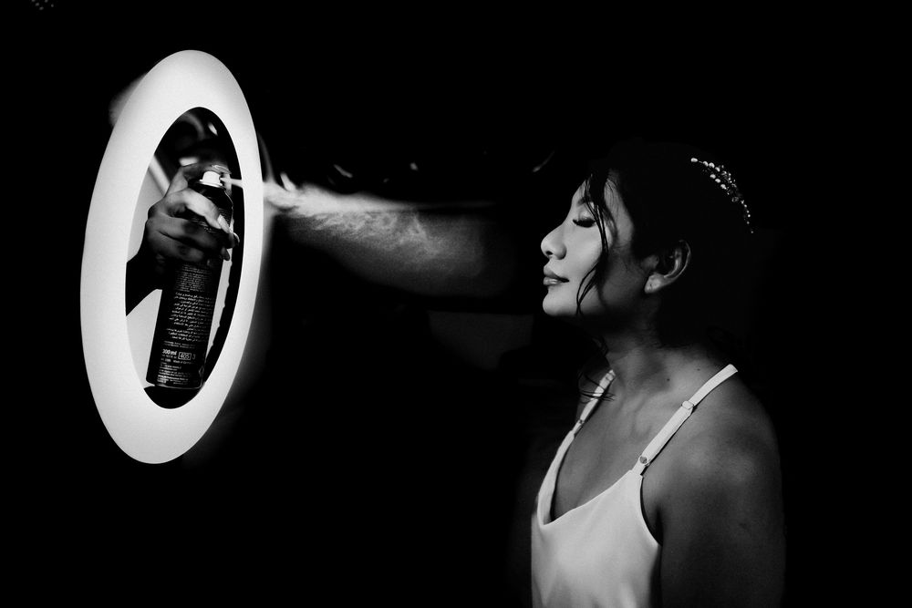 Black and white photo of a person spraying aerosol near a illuminated circular mirror in dramatic lighting.