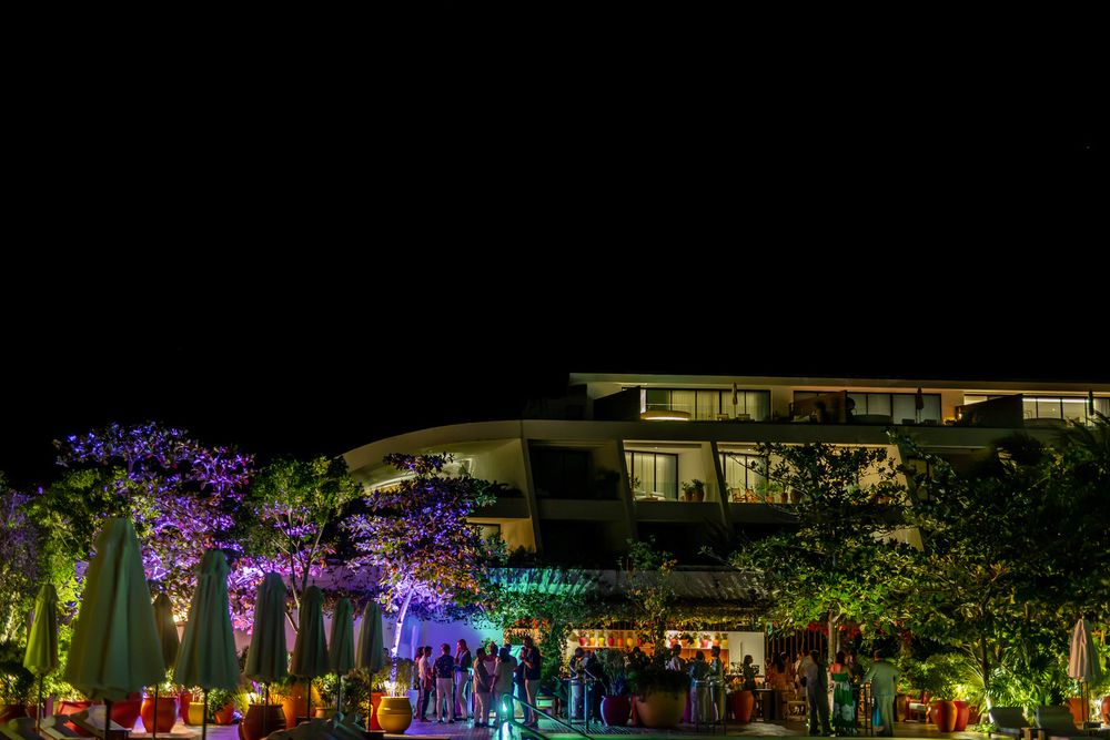 Colorful night event at a modern venue with purple-lit trees and crowds gathered outside under dark sky.