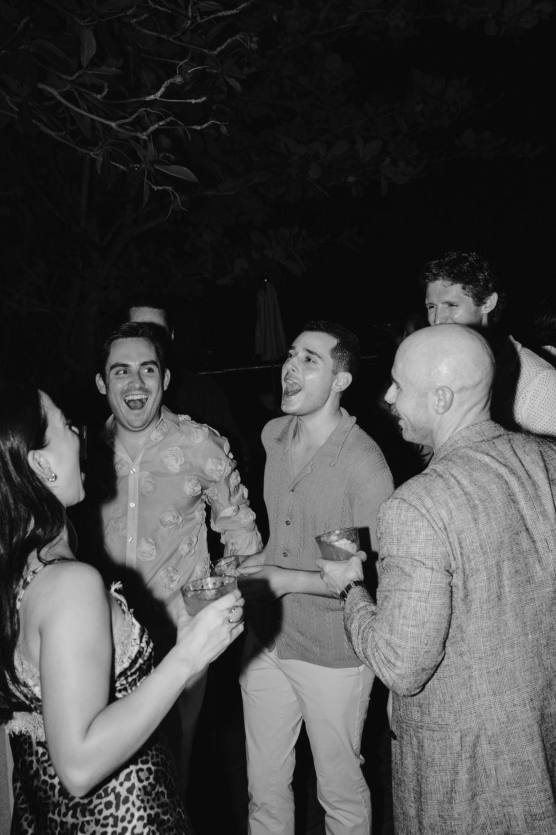 Group of friends laughing and holding drinks at an outdoor nighttime party celebration.