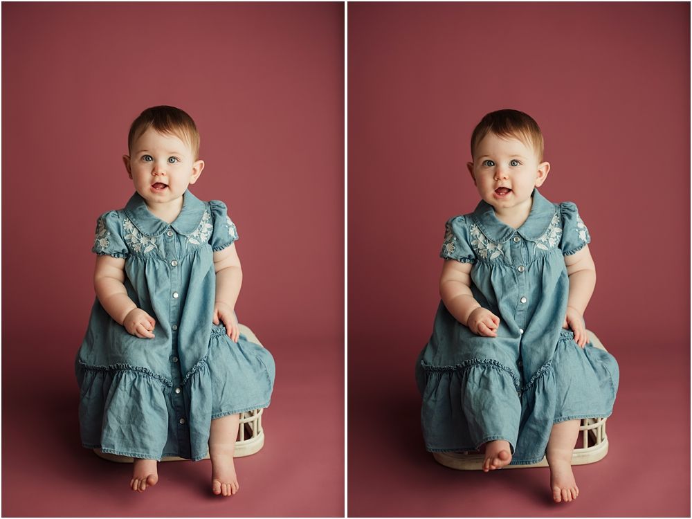 Baby in teal dress sits on wooden stool against pink backdrop in professional studio portrait photography.