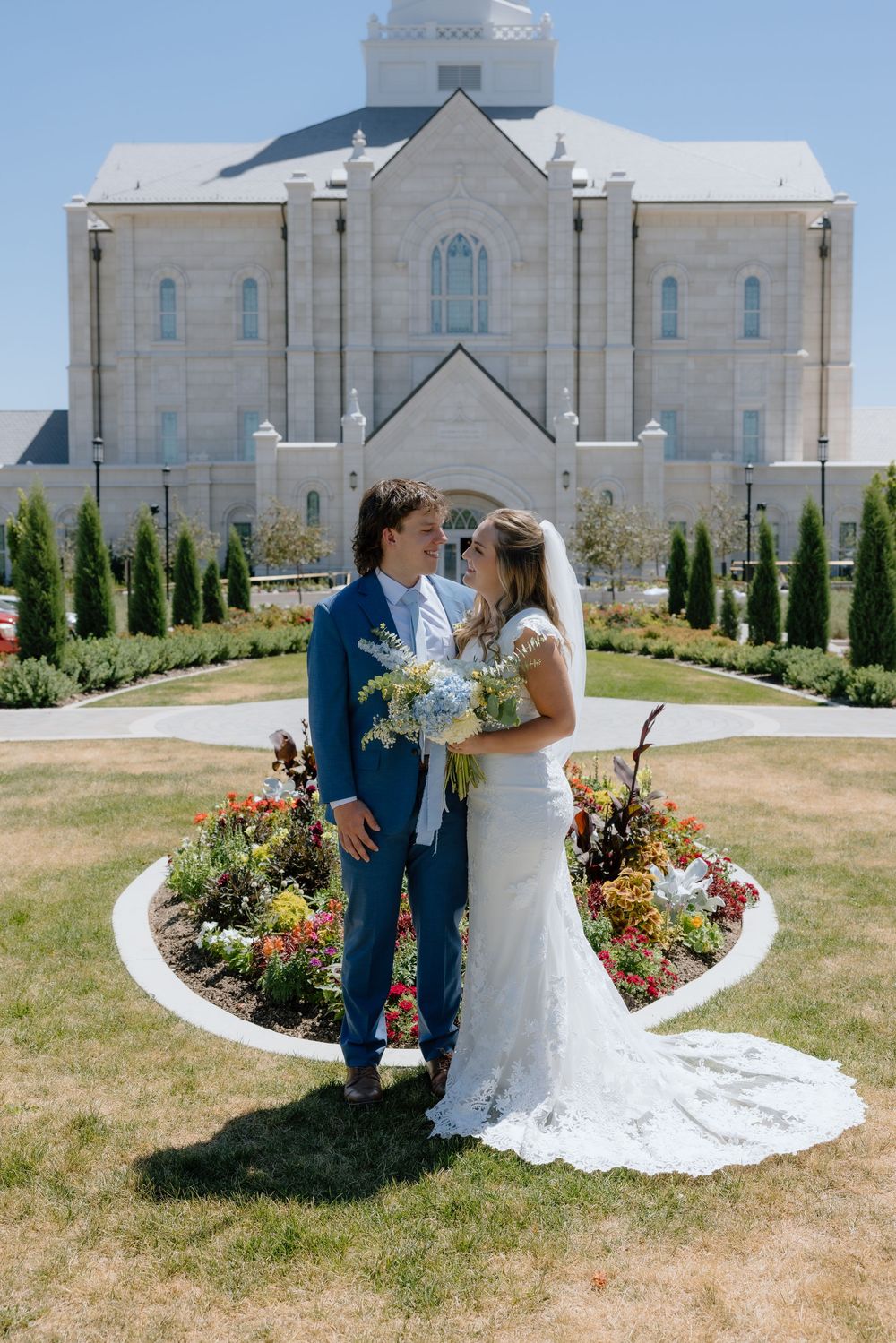 Bride and groom gazing at each other in a circular flower garden in front of an LDS temple.