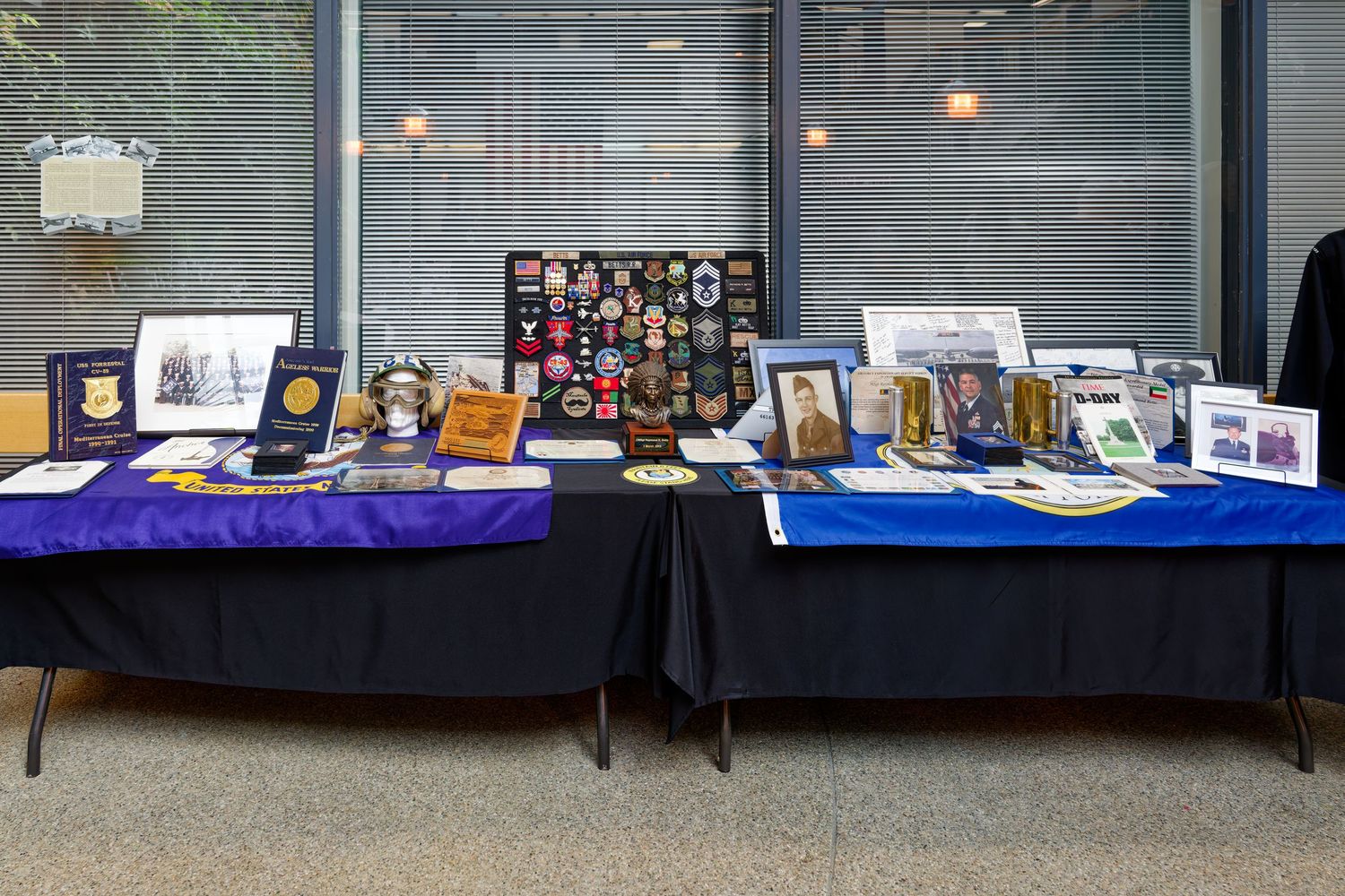 Military memorabilia display table with patches, photos, medals, and insignia on black tablecloth.