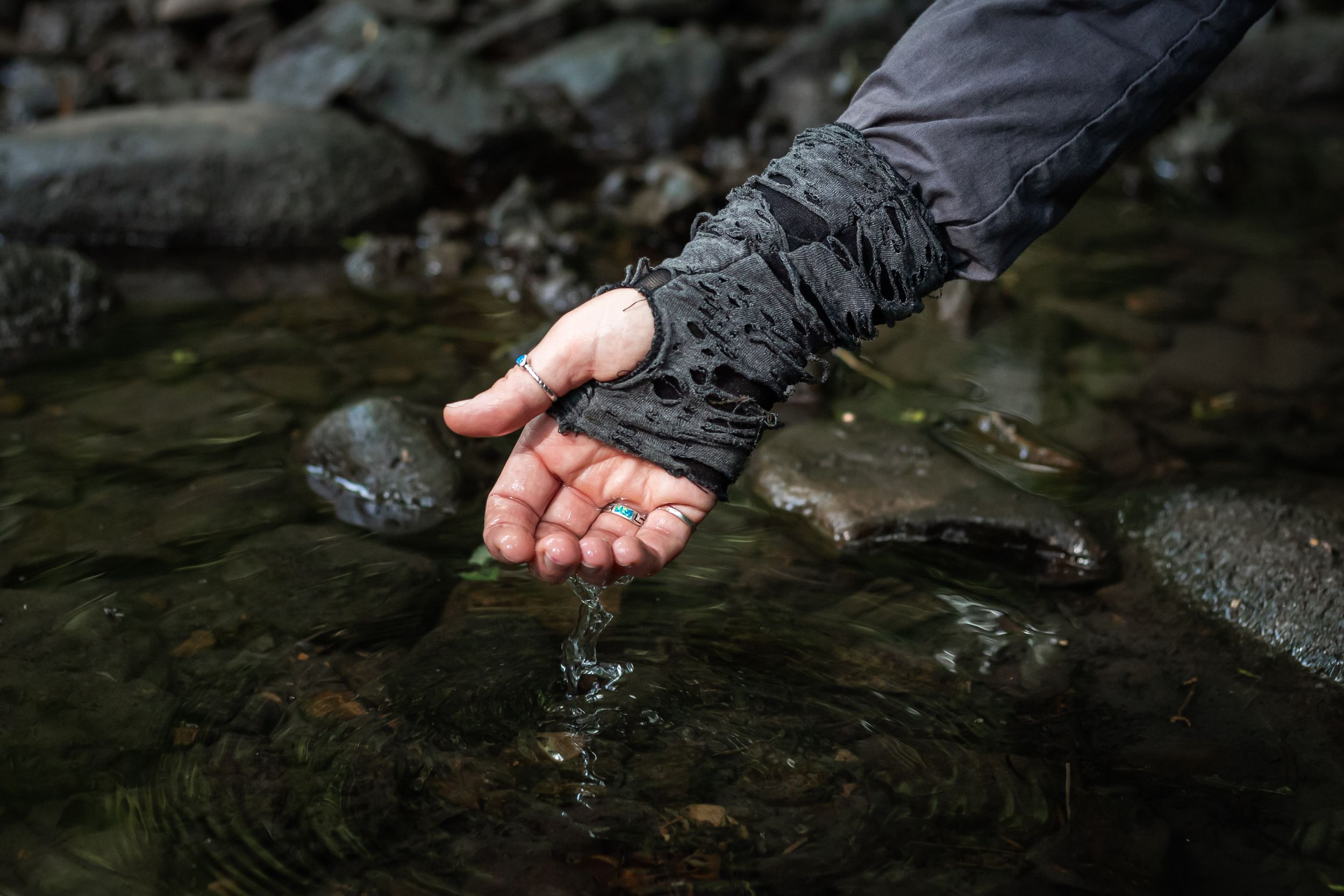 A hand cupping clear stream water over rocky riverbed in nature.