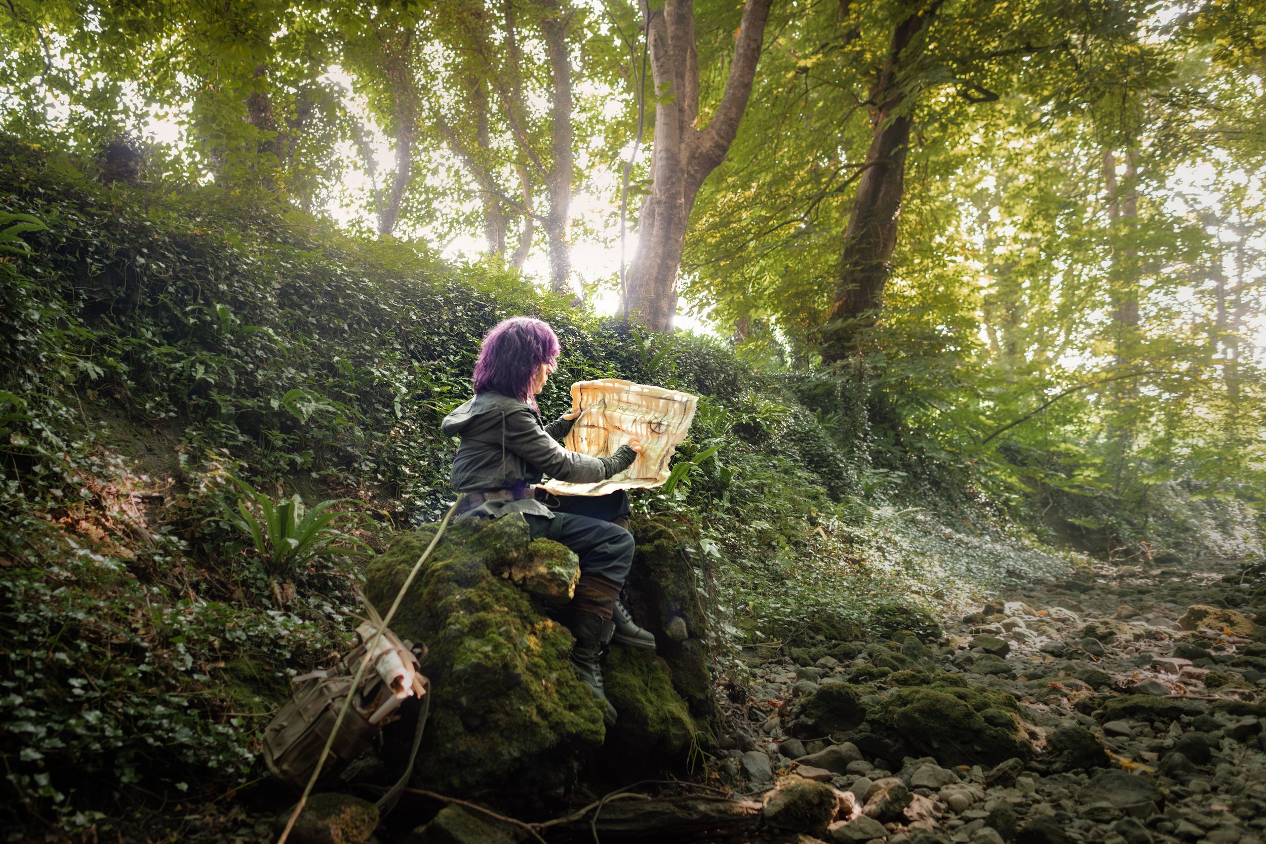 Child reading a map on mossy rocks in a sunlit enchanted forest surrounded by lush green ivy and trees.