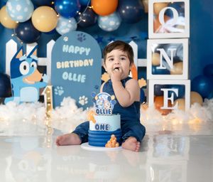 Baby boy Ollie celebrates his first birthday with a Bluey-themed cake smash, surrounded by blue and gold balloons.